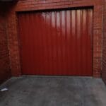 Professionally spray painted glossy red metal roller garage door framed by classic red brickwork by S and R Painting Group in Clayton and Chadstone.
