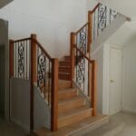 Professionally stained internal timber staircase featuring white balustrades and decorative wrought iron details by S and R Painting Group in Mount Waverley.