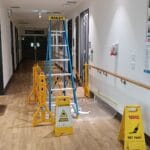 Commercial interior hallway wall painting preparation with ladders and safety signs by S and R Painting Group in Clayton and Mulgrave.