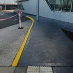 Professionally applied yellow safety line marking and grey concrete coating on an outdoor commercial walkway by S and R Painting Group in Dandenong and Moorabbin.
